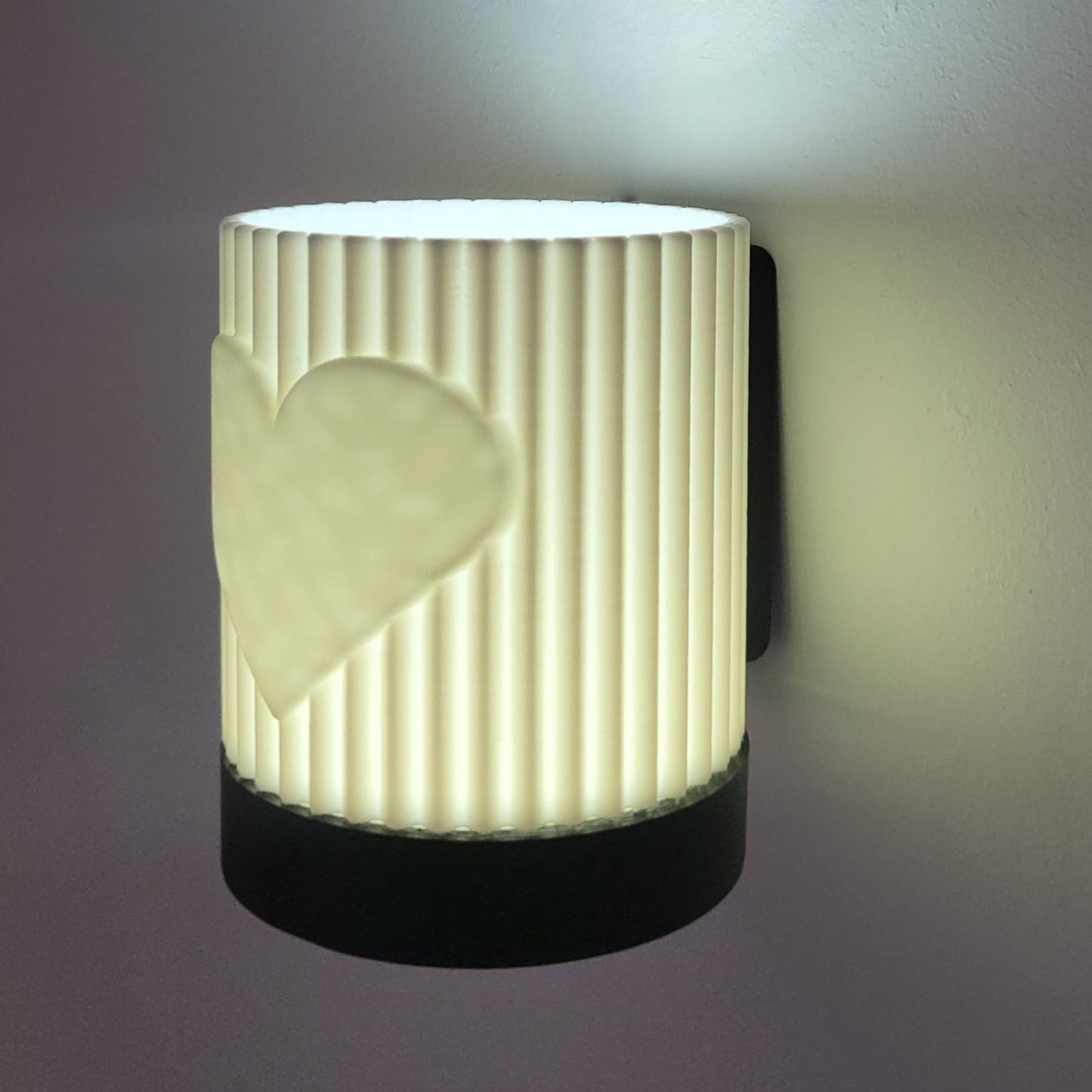 Wall-mounted light fixture with ribbed design and heart cutout on a dark background