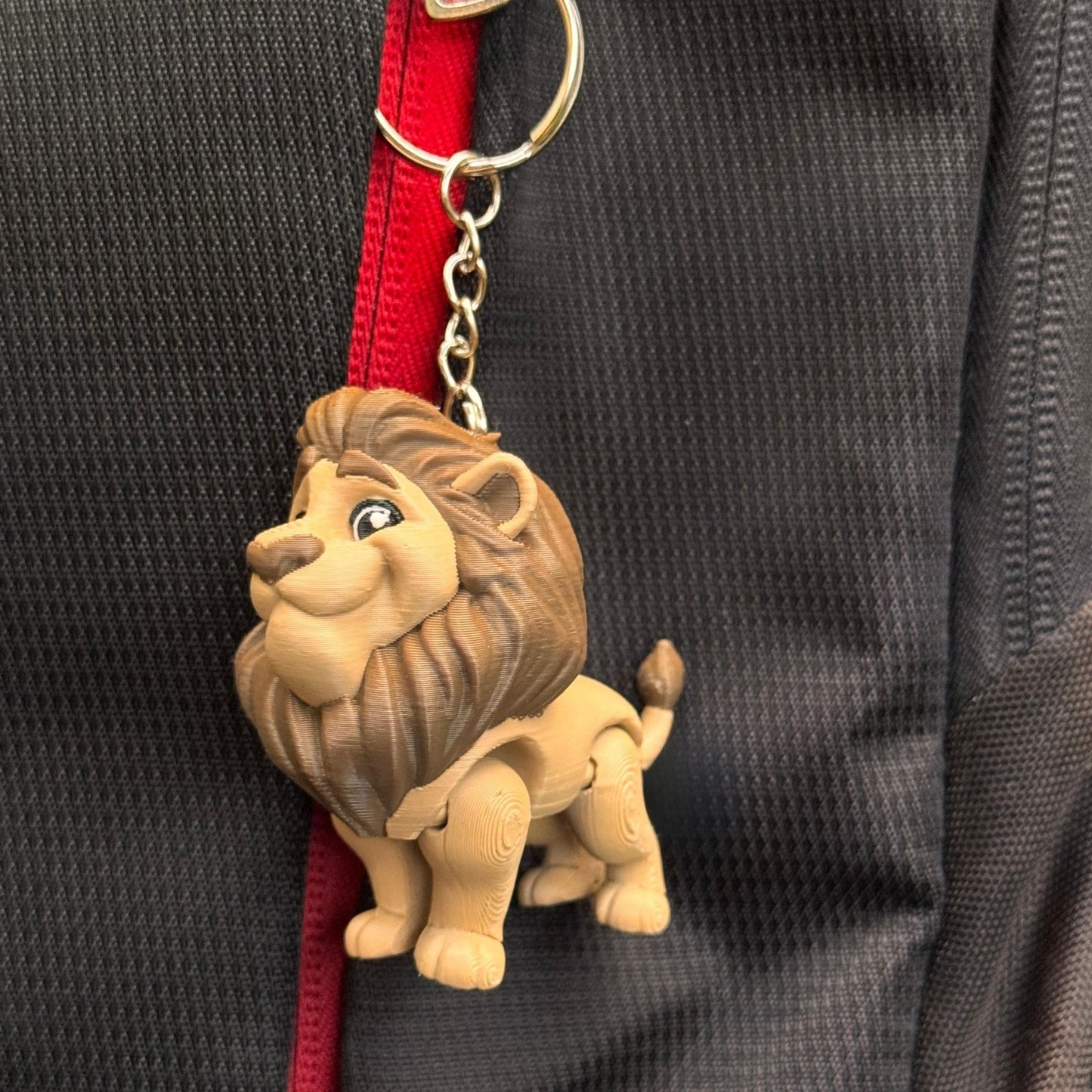 A whimsical lifestyle shot shows the lion couple keychains on a desk beside a notebook, a cup of tea, and a small potted plant. The scene evokes creativity and comfort, perfect for someone who enjoys fun, meaningful desk accessories.
