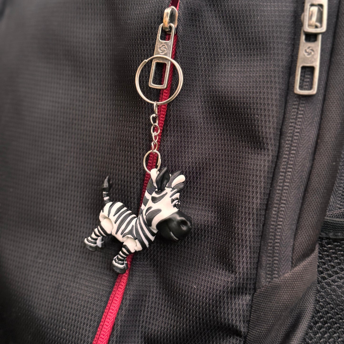 Zebra keychain hanging from a backpack zipper, showing the high-detail 3D-printed finish and playful safari theme.