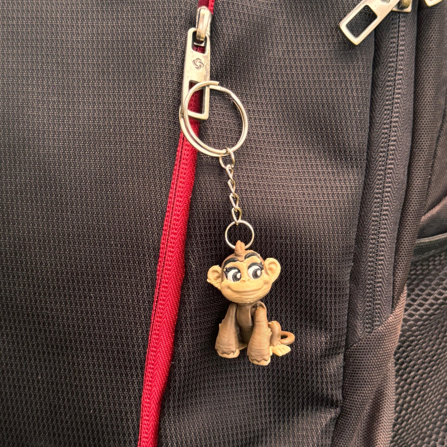 The monkey keychain lies next to everyday objects like coins, keys, and a pen to show scale; its compact size makes it ideal for pockets, bags, or keyrings.