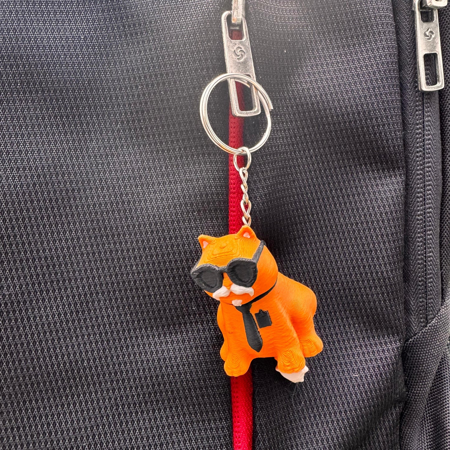 Orange cat keychain in a close-up shot that emphasizes the sunglasses and necktie. Its bright color and cool expression make it eye-catching.