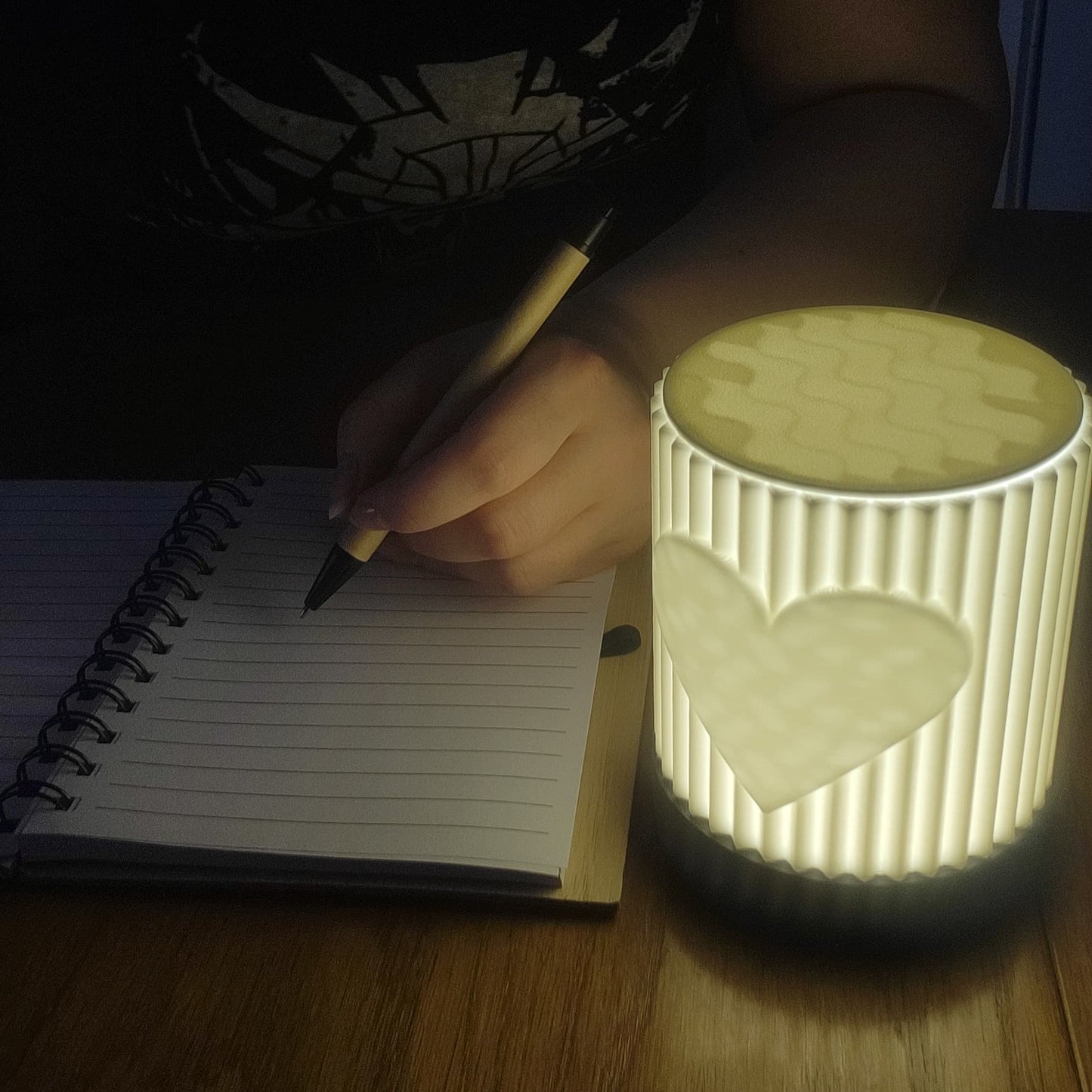 Person writing in a notebook next to a heart-shaped night light