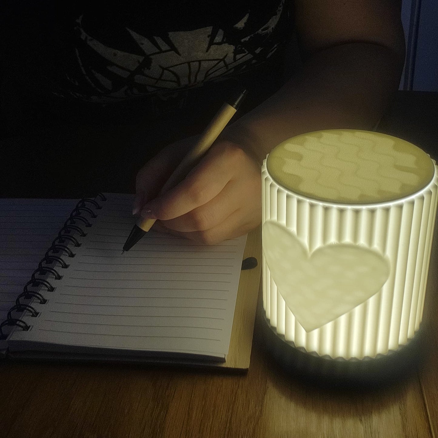Person writing in a notebook with a lit night light on a wooden surface