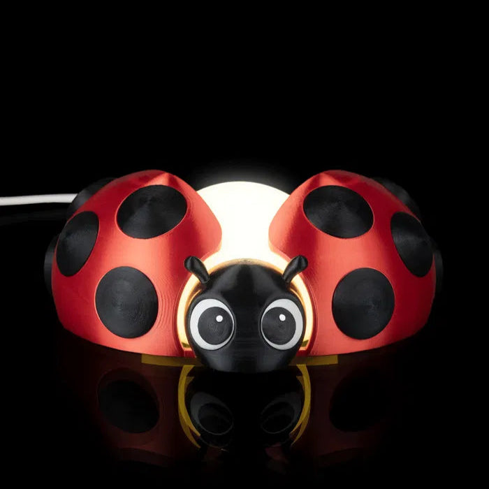 Toy ladybug with a black body and red shell on a reflective surface.