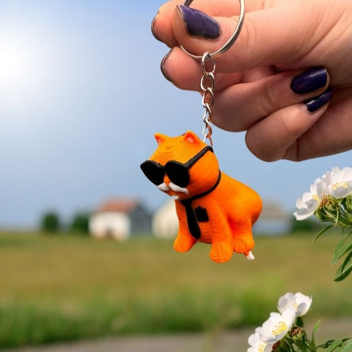 Orange cat keychain viewed from above, placed next to a notebook and pencil. Perfect for students who love fun, animal-themed accessories.