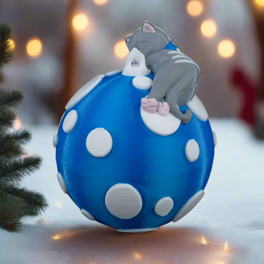 Blue ball with white polka dots and a gray cat figurine on a black background
