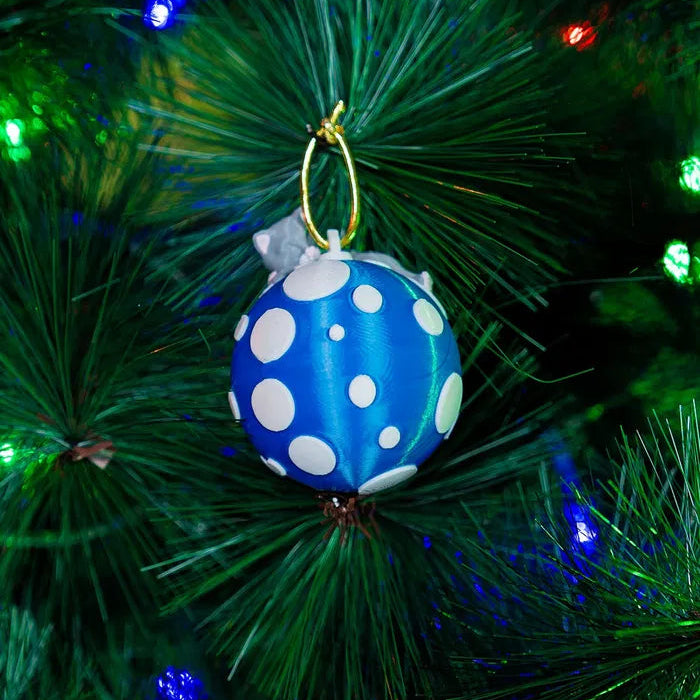 A 3D printed blue Christmas tree decoration featuring a sleeping cat on a globe, hanging on a Christmas tree with multicolored lights.