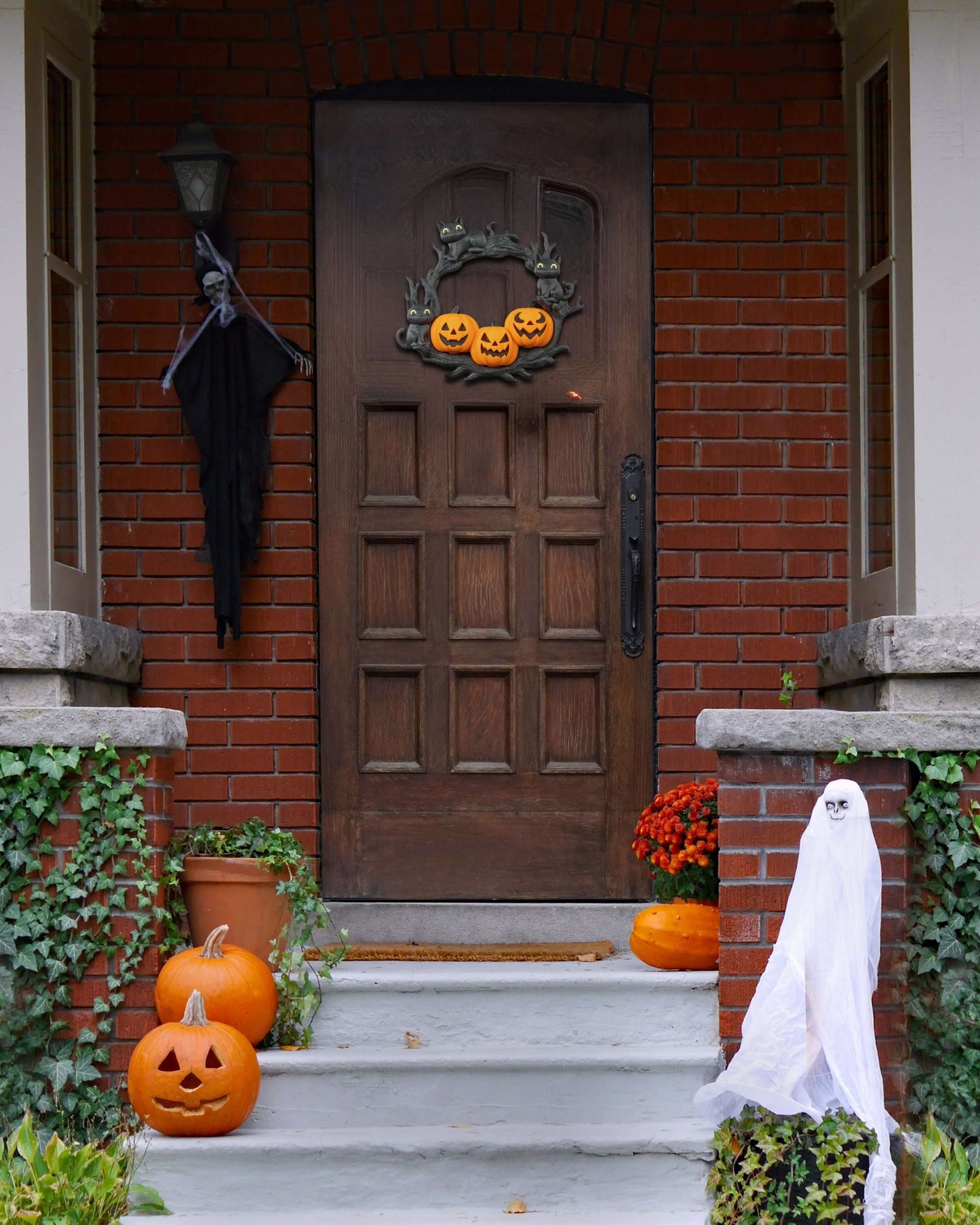 Halloween decorations on a house entrance with pumpkins, ghosts, and a broom.