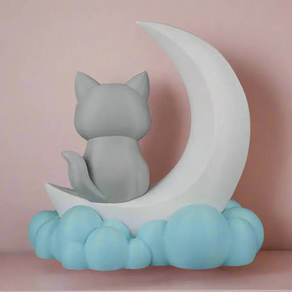 Decorative figurine of a cat sitting on a crescent moon with clouds below, on a black background.