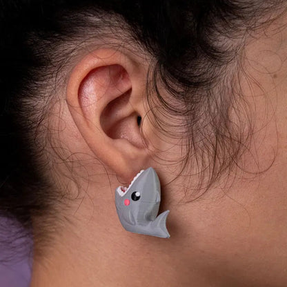 Close-up of a hand holding one shark earring against a rollercoaster in the distance — theme park chaos & fun.