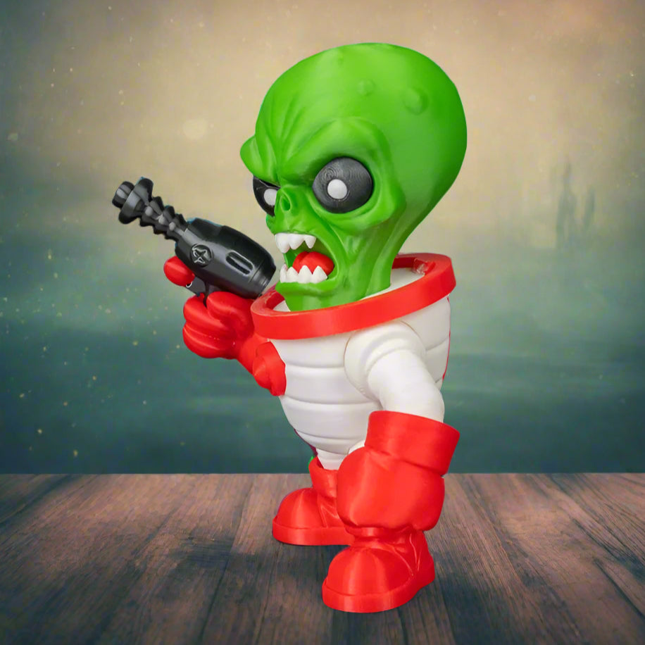 Toy figure of a green alien with red boots and white suit holding a black gun on a black background