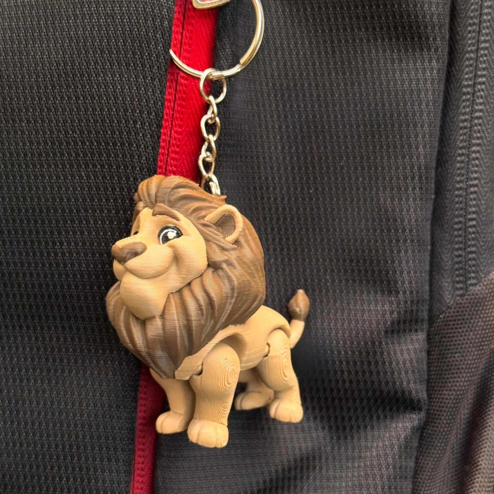 A whimsical lifestyle shot shows the lion couple keychains on a desk beside a notebook, a cup of tea, and a small potted plant. The scene evokes creativity and comfort, perfect for someone who enjoys fun, meaningful desk accessories.