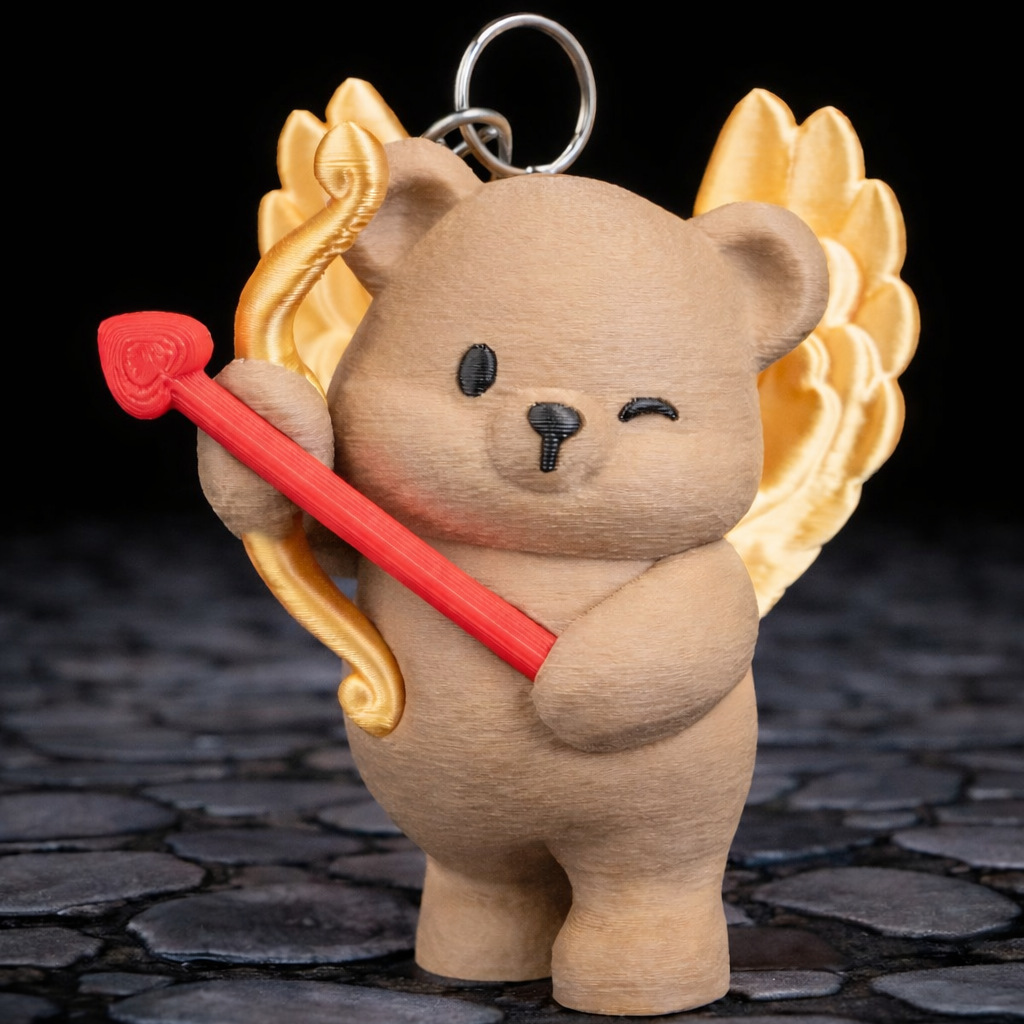 Teddy bear keychain with wings and a red heart on a dark stone surface