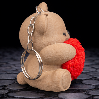 Keychain shaped like a bear holding a red heart on a dark textured surface