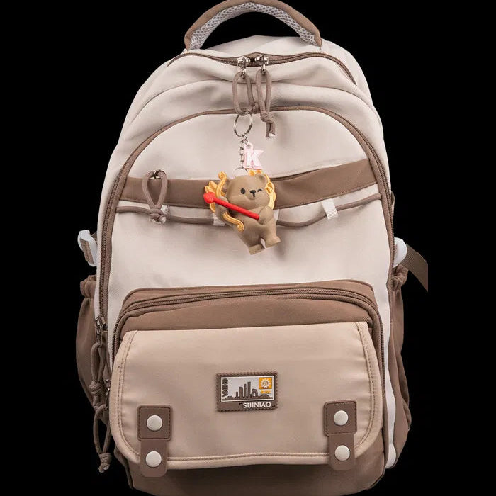 Beige backpack with a teddy bear charm on a white background