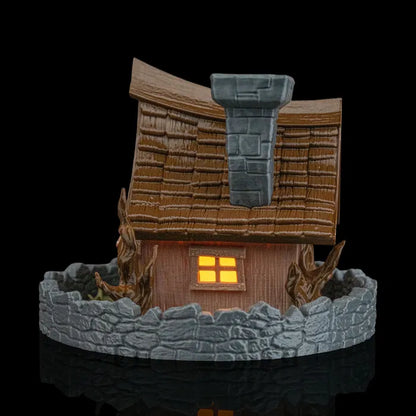 Small model of a thatched-roof cottage with a lit window on a black background