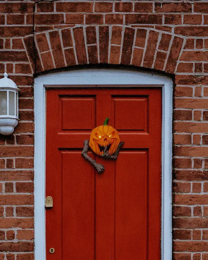 Red door with a Halloween pumpkin knocker on a brick wall.