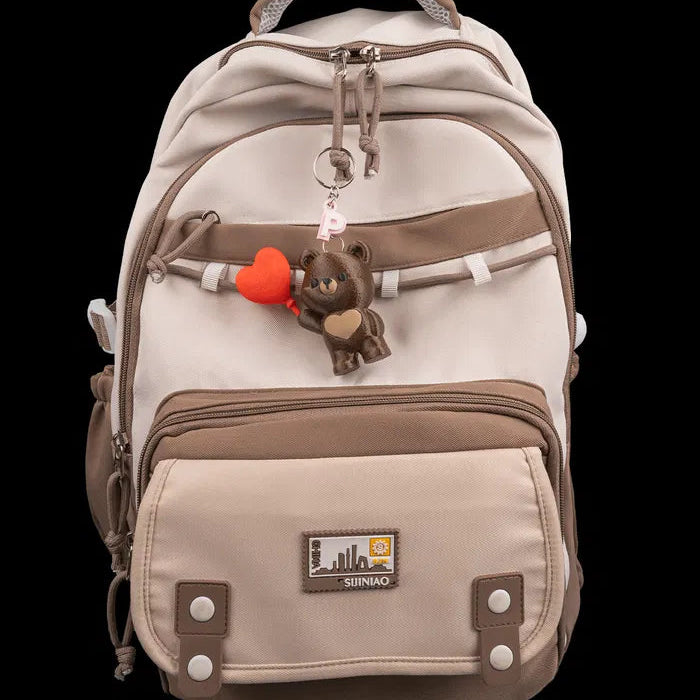 Beige backpack with brown accents and a keychain on a white background