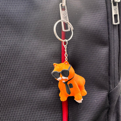 Orange cat keychain in a close-up shot that emphasizes the sunglasses and necktie. Its bright color and cool expression make it eye-catching.