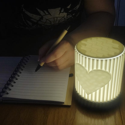 Person writing in a notebook with a lit night light on a wooden surface