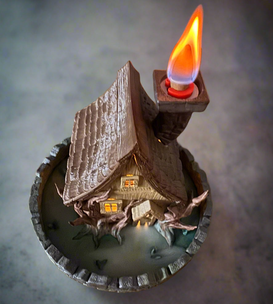Decorative candle shaped like a miniature house with a lit flame on a gray background