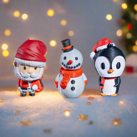 Three Christmas-themed figurines (Santa, snowman, penguin) on a snowy surface with blurred lights in the background.