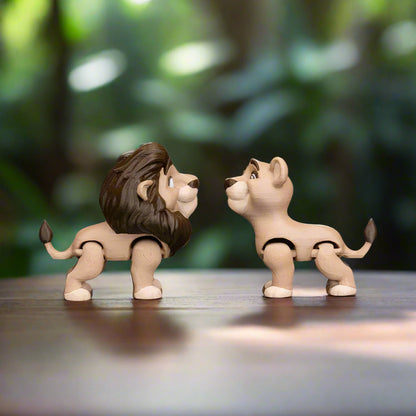 A hand holds the lion couple keychains, fingers curled around the key ring, highlighting how small and portable the accessories are. The bright lighting makes the playful textures and patterns on each lion pop, inviting a closer look.