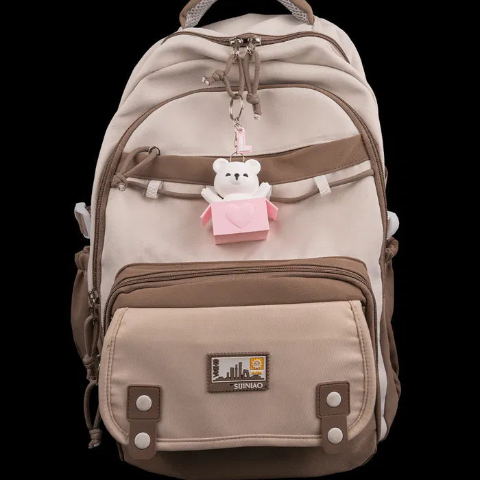 Beige and brown backpack with a teddy bear charm on a black background