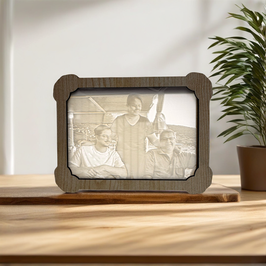 Wooden photo frame with engraved picture of three people on a wooden surface with a plant in the background.
