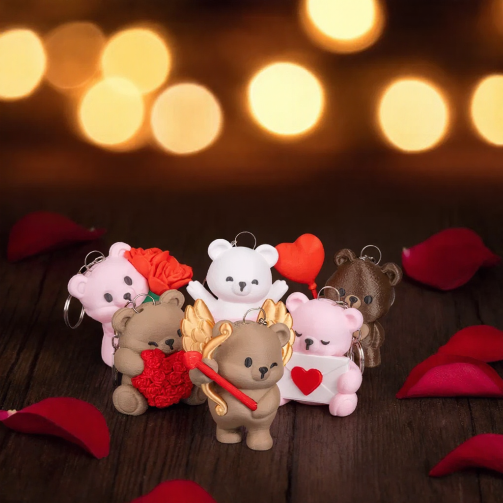 Small teddy bear keychains with heart and rose designs on a wooden surface with blurred lights in the background.