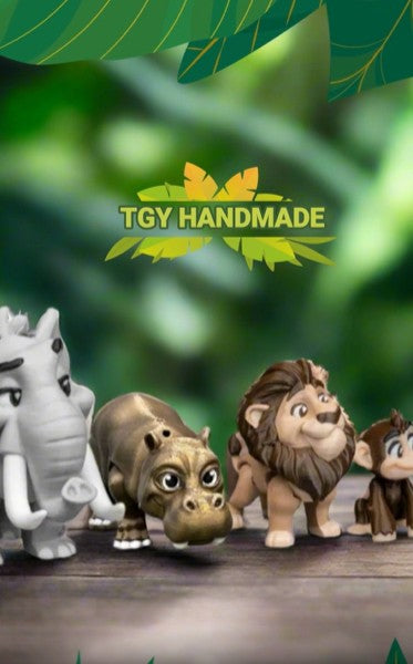 The lion and hippo figurines are posed side by side on a desk next to a mug and a plant, suggesting their use as cute desk companions or cheerful decorative items.
